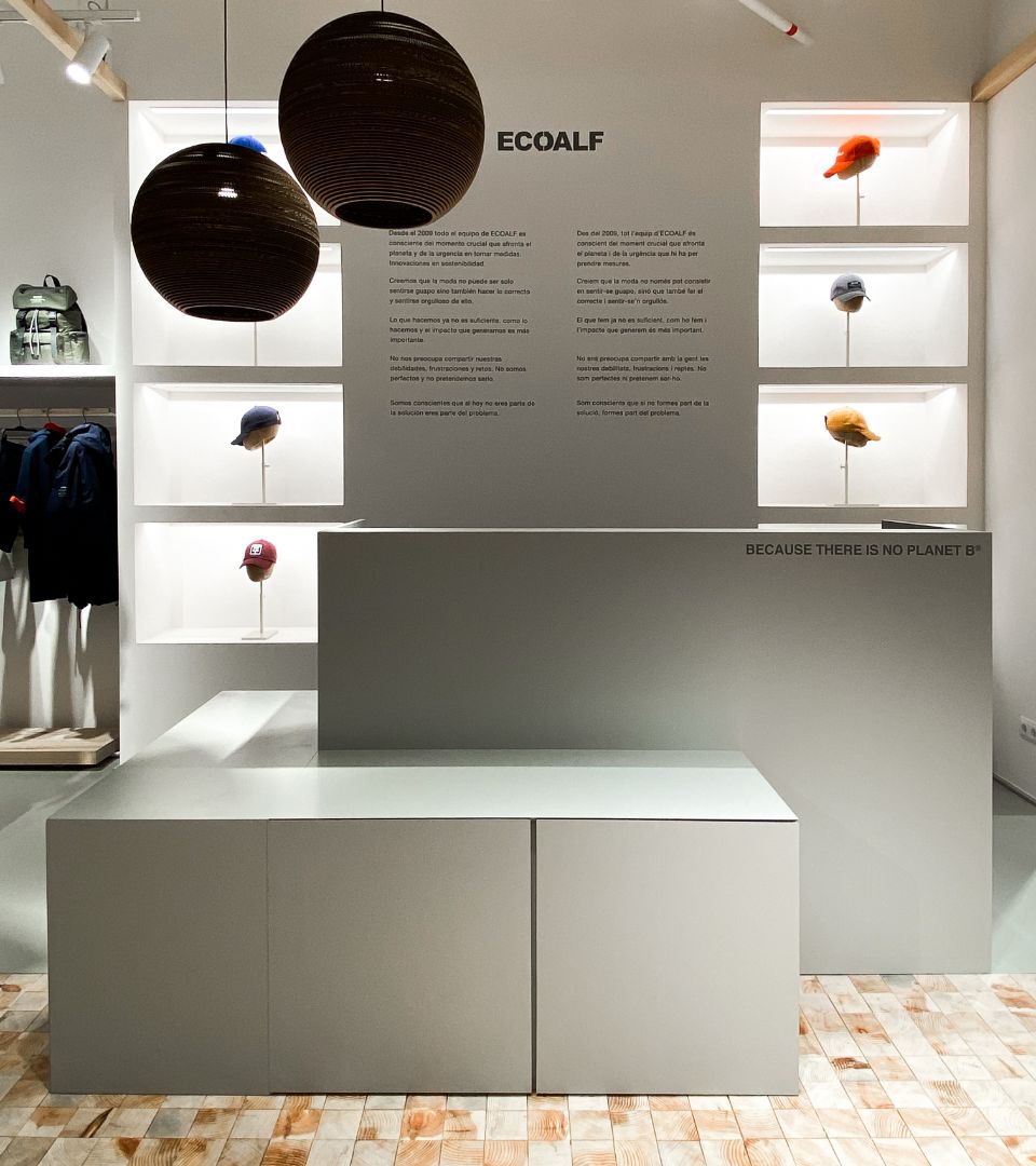 Escaparate de tienda Ecoalf con una selección de gorras y prendas de moda circular en un entorno minimalista.
