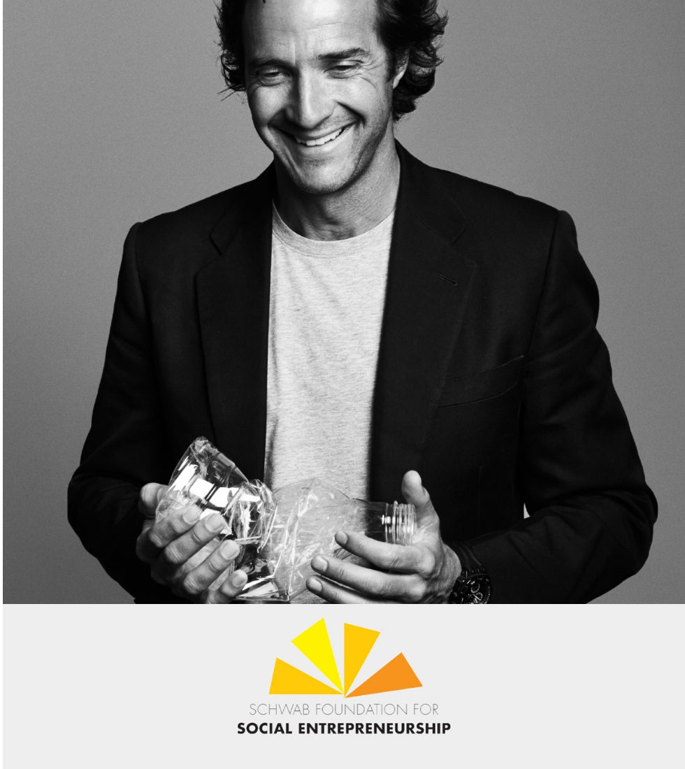Un hombre con camiseta clara y chaqueta oscura sostiene una botella de plástico reciclable; abajo, el logo de "Schwab Foundation for Social Entrepreneurship".