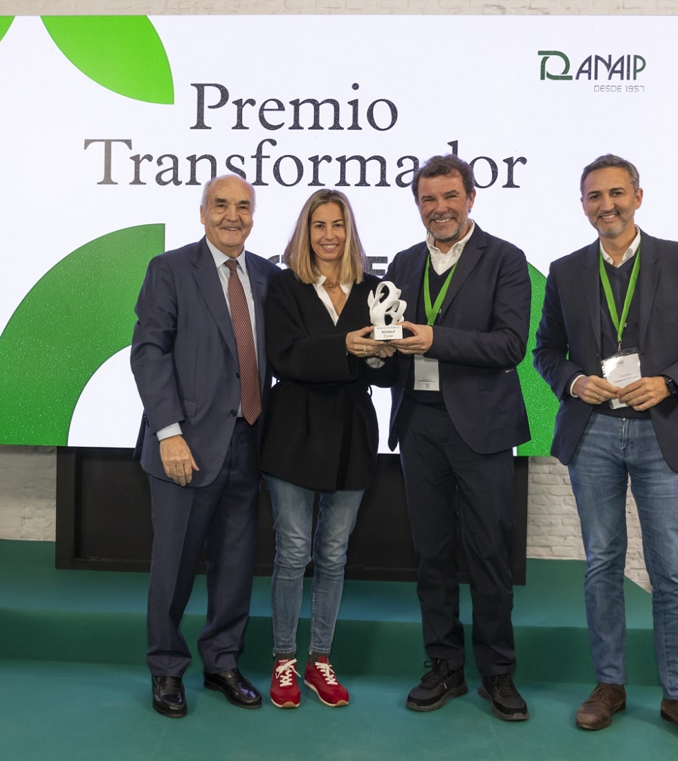 Cuatro personas en un escenario; una mujer y un hombre sostienen un trofeo blanco bajo un cartel que dice "Premio Transformador".