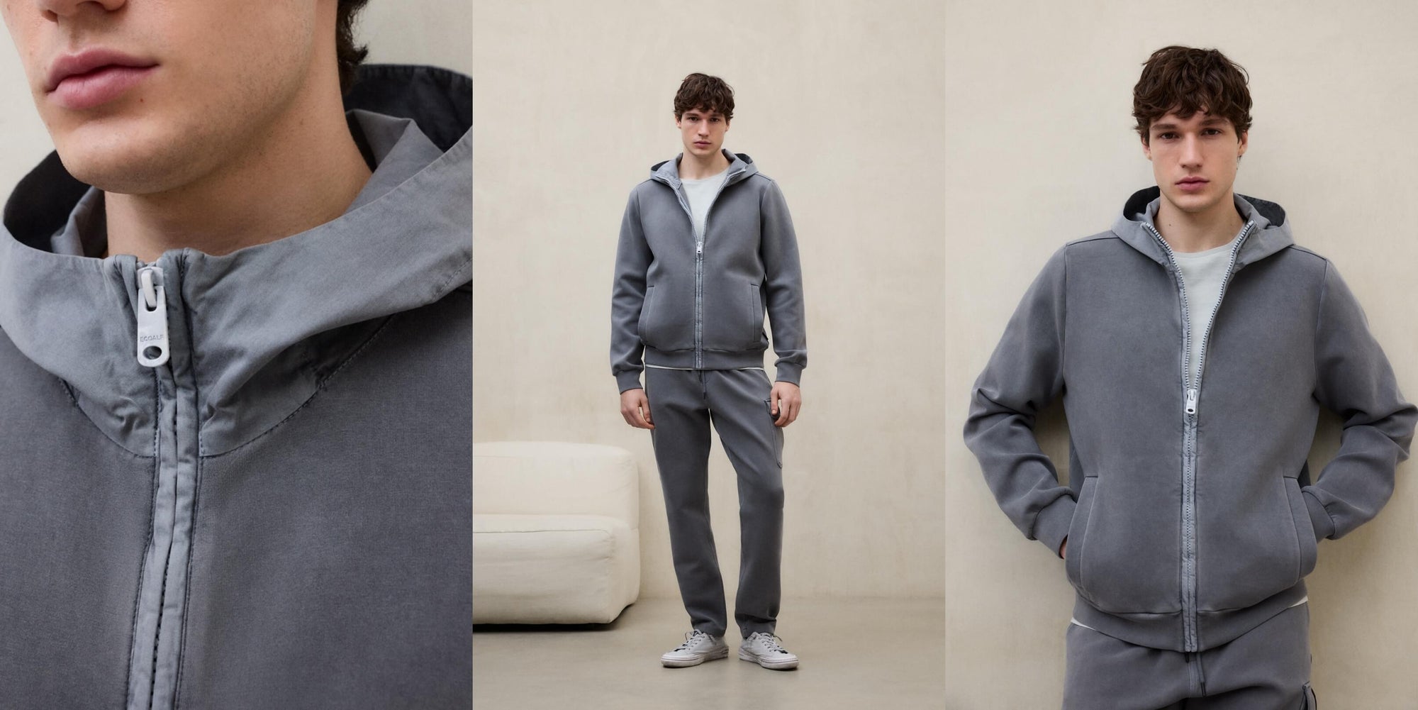 Un hombre con un chándal gris de sudadera de Ecoalf con capucha y pantalón, junto a un sofá blanco en una sala en tonos claros.