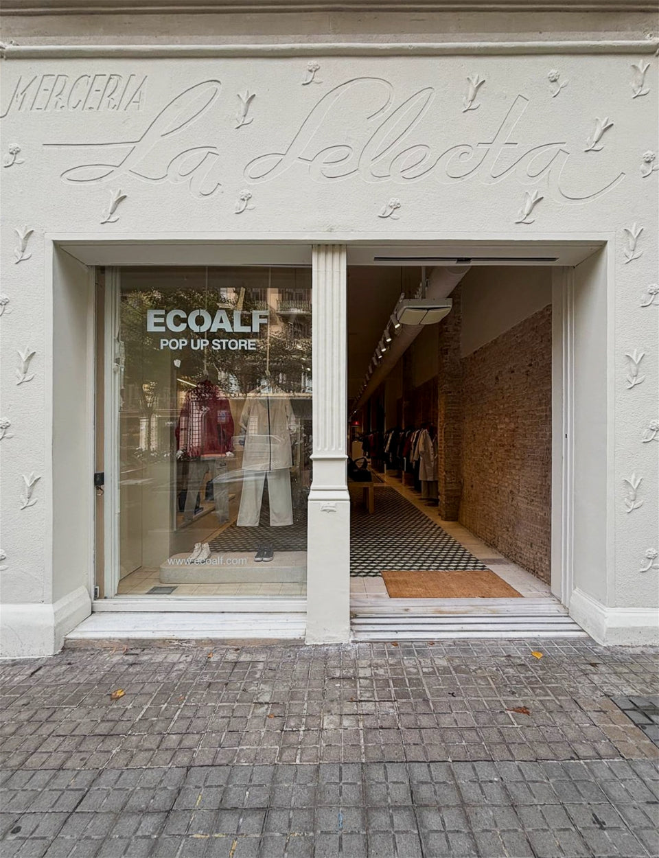 Escaparate y entrada de la "Ecoalf Pop Up Store" en un edificio blanco con el rótulo "La Selecta"; dentro se ve ropa colgada y un suelo de baldosas en blanco y negro.