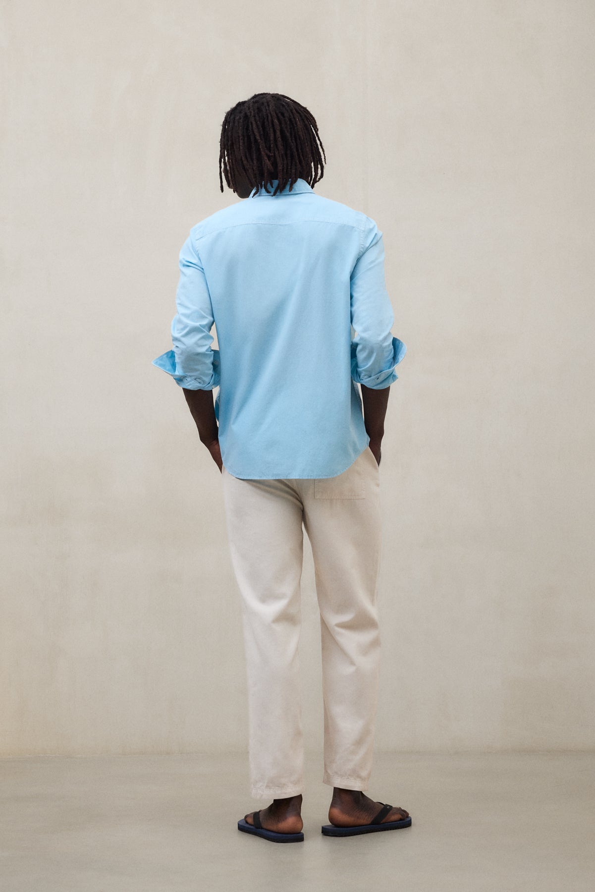 Un hombre de espaldas con camisa azul de la marca Ecoalf y pantalón claro de bajo impacto ambiental.
