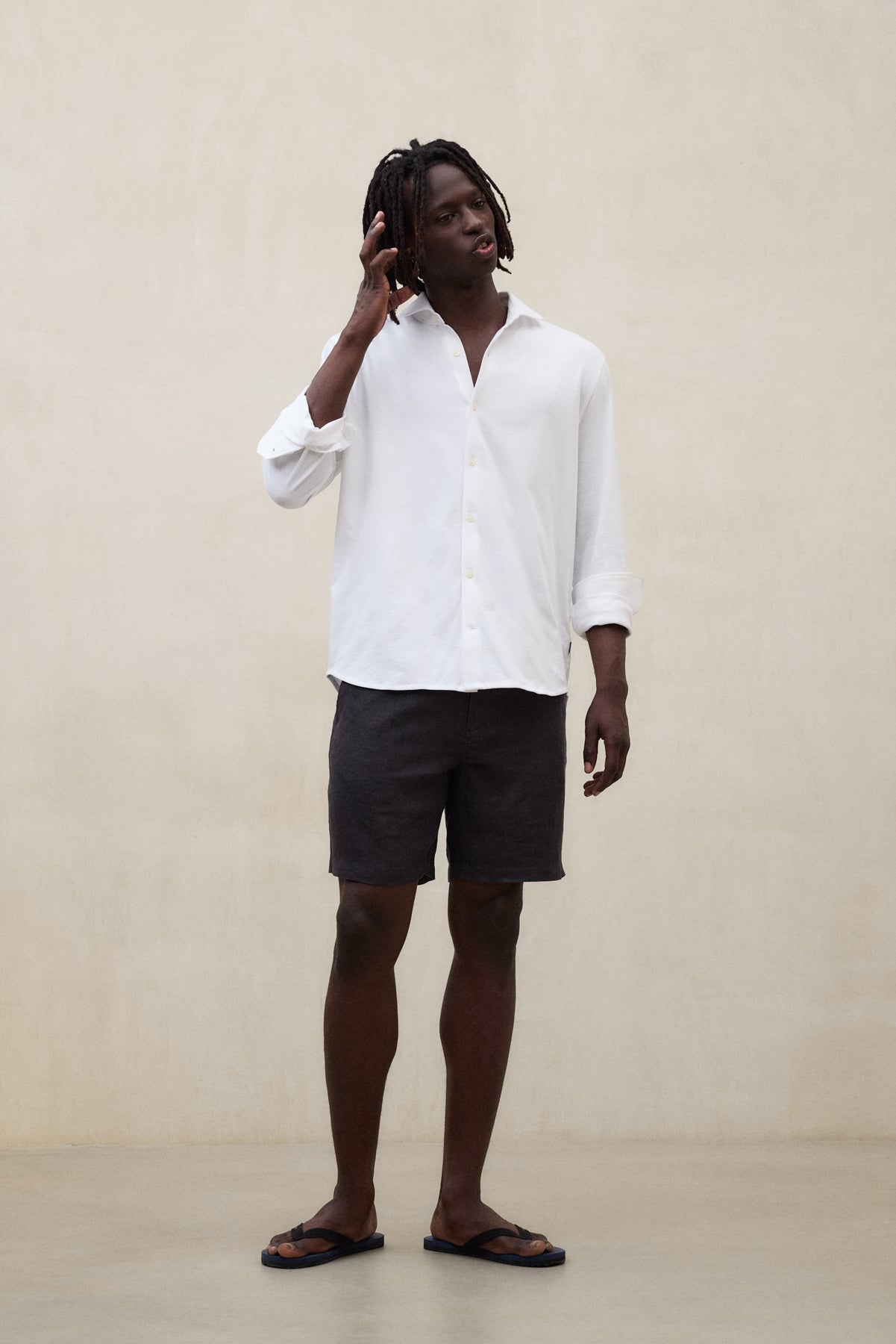 Un hombre con camisa de Ecoalf blanca de manga larga y shorts oscuros, en una sala minimalista.