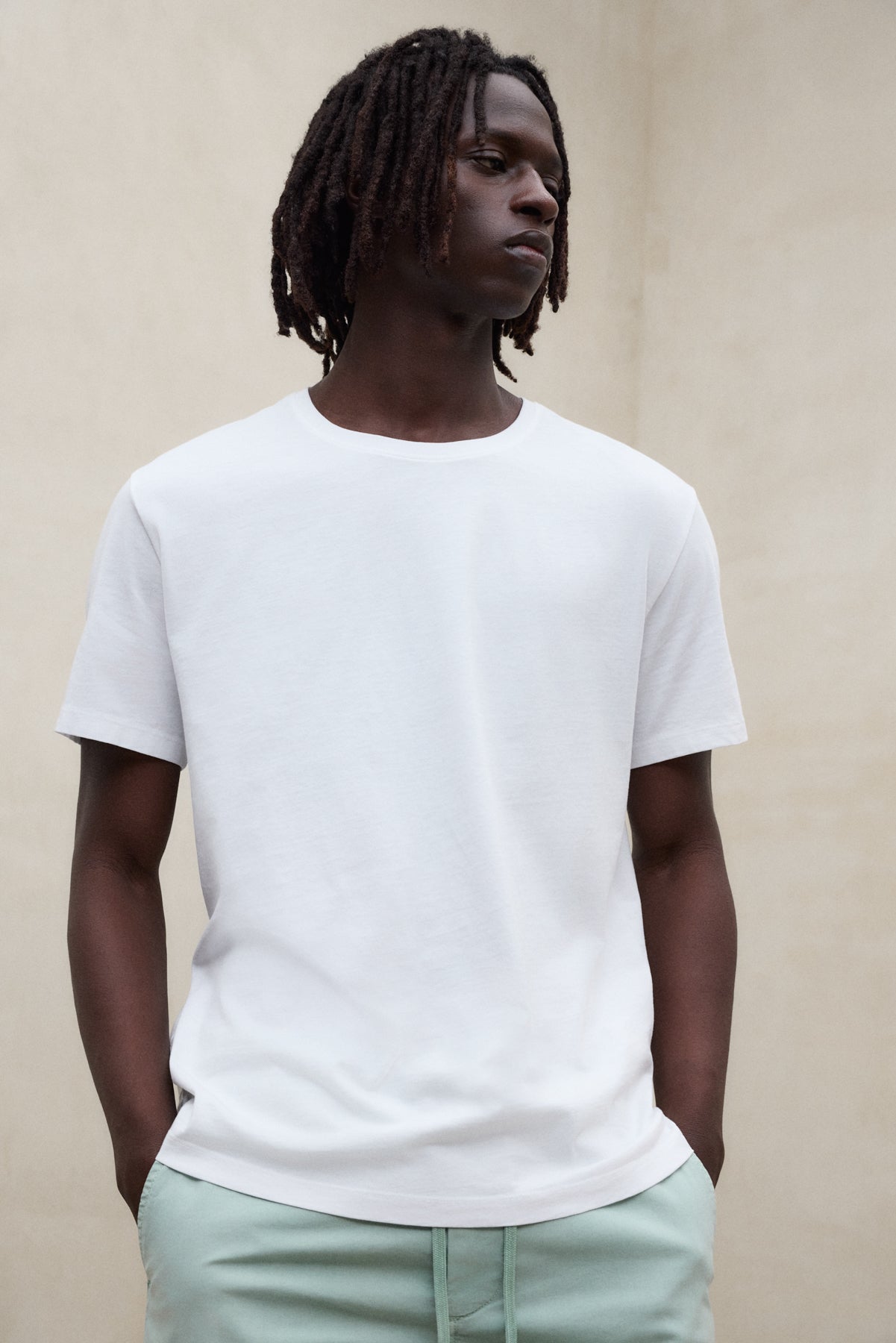 Camiseta blanca básica para hombre de la marca ecoalf.livebinada con pantalón verde claro de fibras sostenibles.