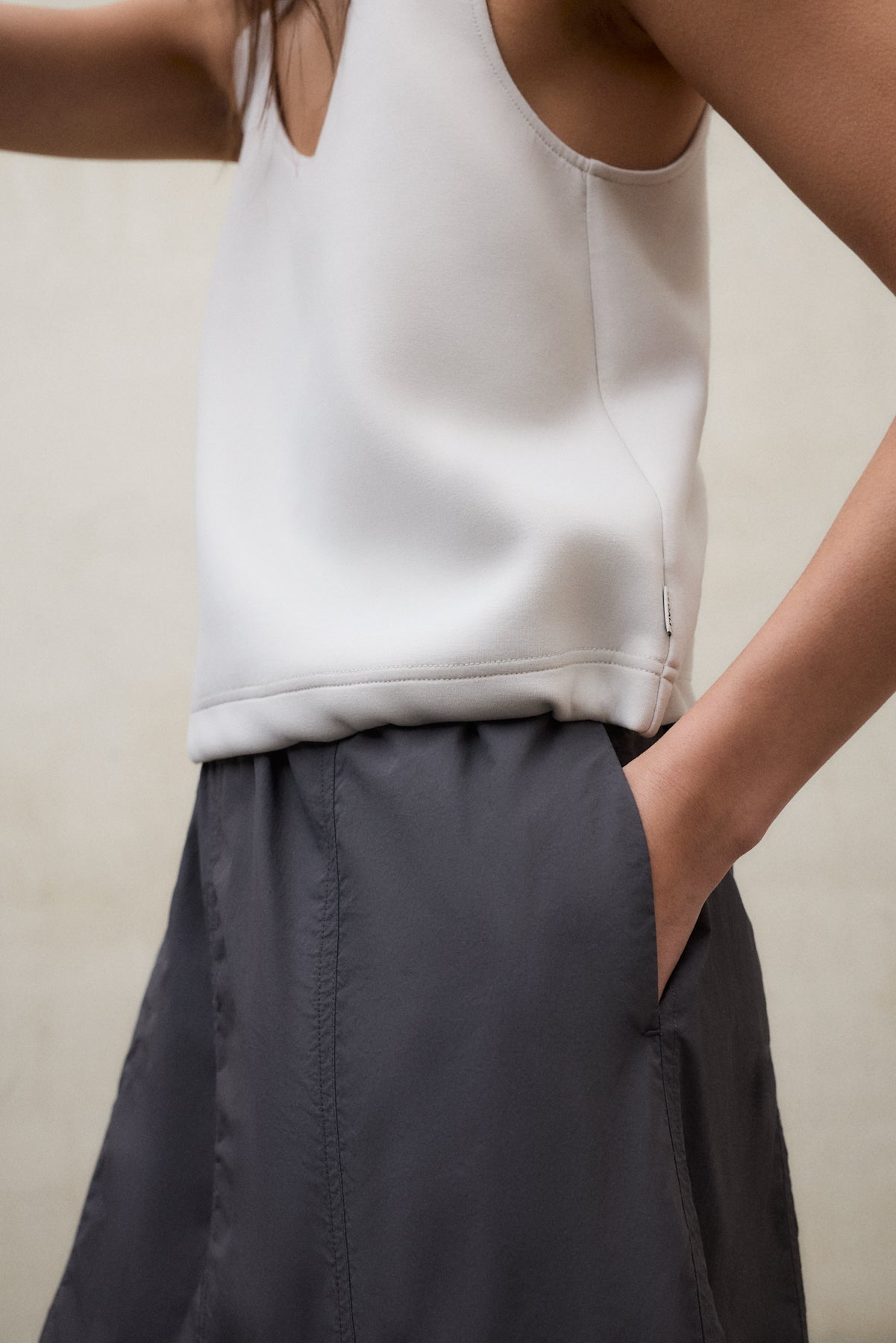 Primer plano de un vestido de Ecoalf blanco con una falda gris oscuro, con la mano en el bolsillo, sobre fondo neutro.