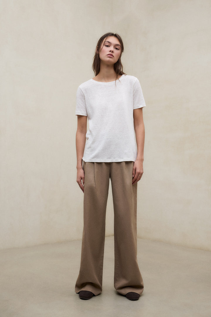 Una modelo vistiendo camiseta blanca y pantalón marrón de fibras sostenibles de la marca Ecoalf.
