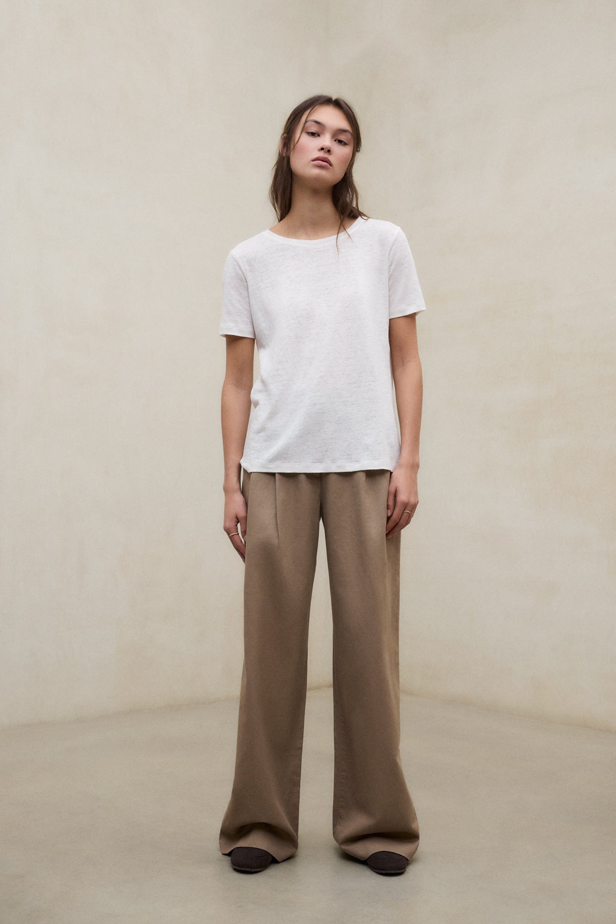 Una modelo vistiendo camiseta blanca y pantalón marrón de fibras sostenibles de la marca Ecoalf.