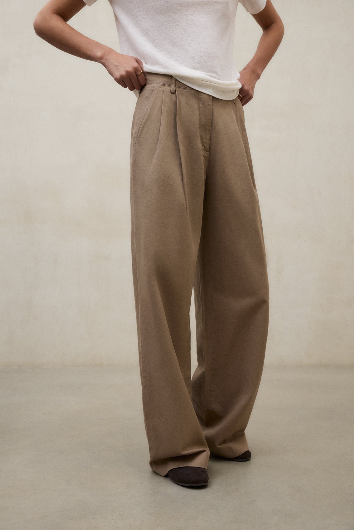 Una persona posando con pantalón ancho beige de bajo impacto ambiental de la firma Ecoalf sobre un fondo neutro.