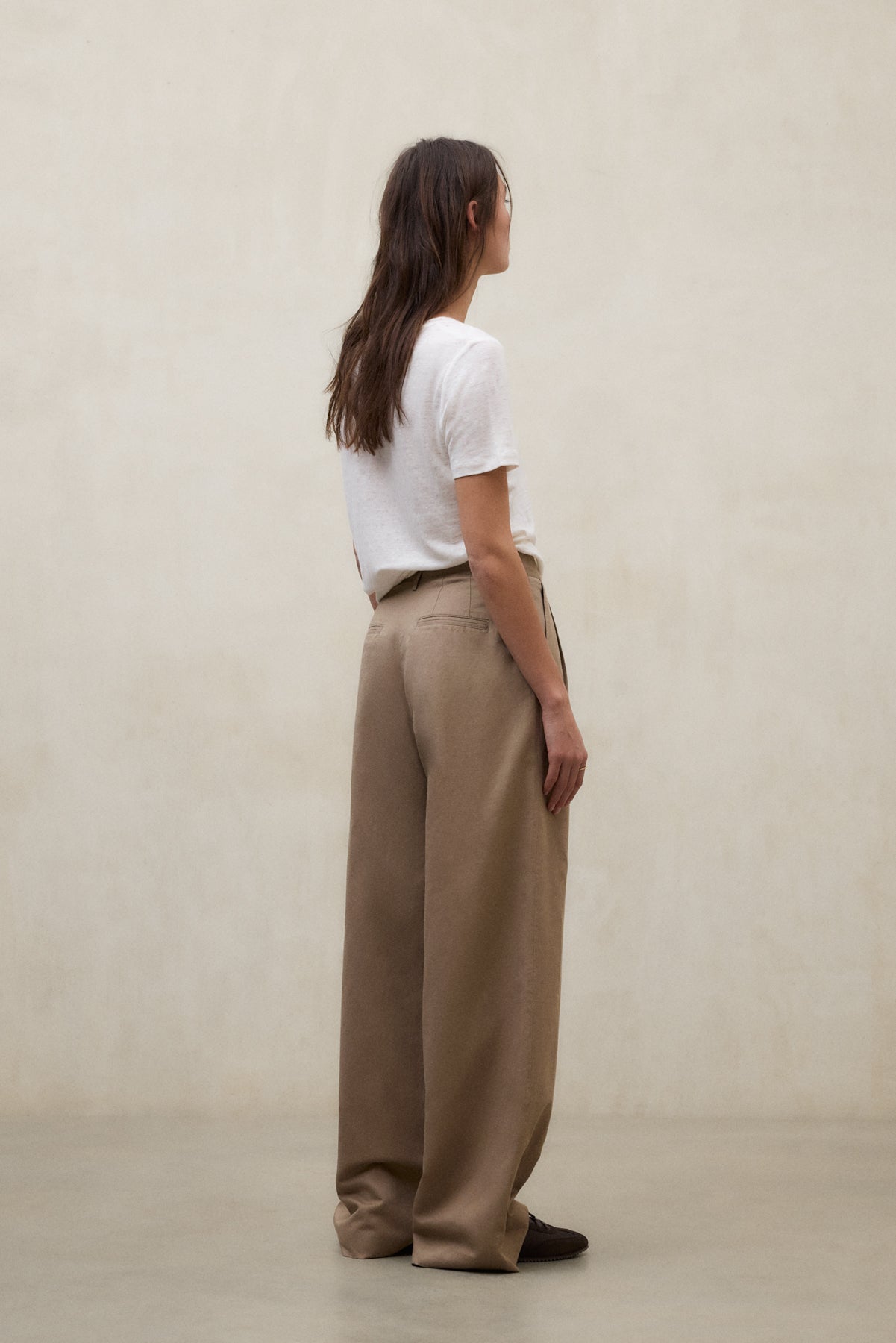 Una mujer con pantalón ancho color camel en tejido sostenible de Ecoalf y camiseta blanca de algodón orgánico.