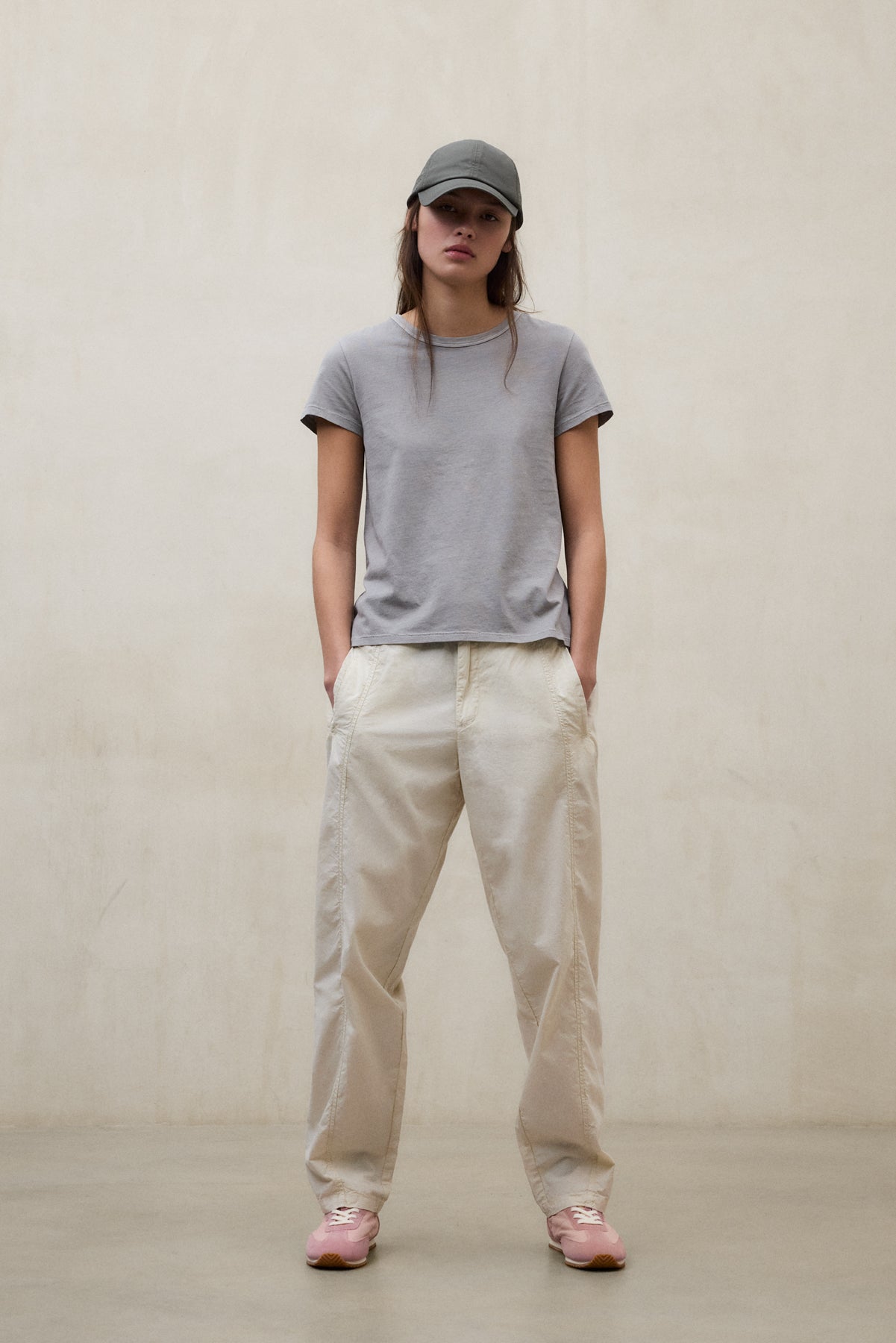 Una mujer vistiendo gorra, camiseta gris, pantalón beige y zapatillas rosas de la marca Ecoalf.