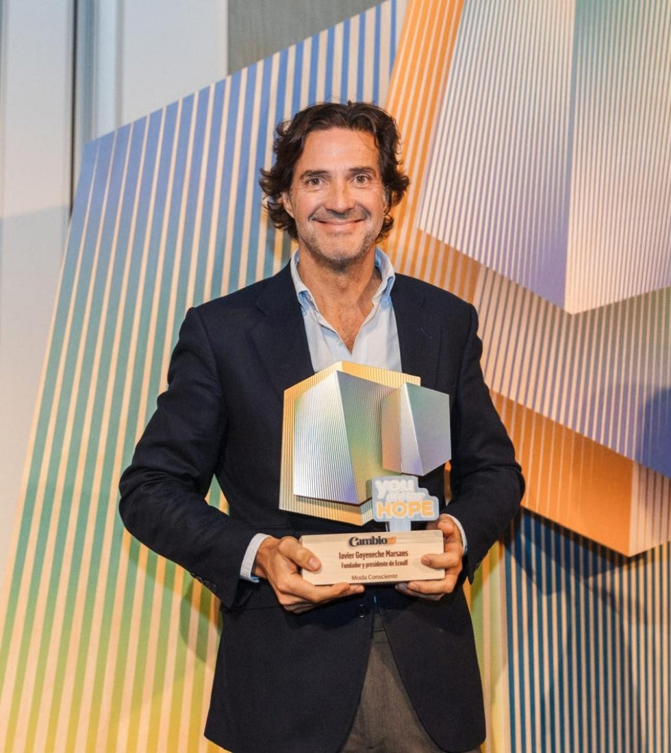 Un hombre con americana oscura y camisa clara sostiene un trofeo, sobre un fondo de líneas diagonales de colores.