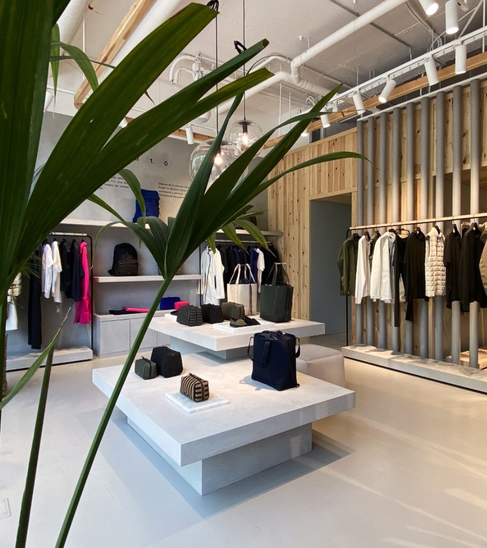 Interior de tienda Ecoalf con ropa y accesorios sobre estanterías de madera y decoración natural en un espacio moderno y minimalista.